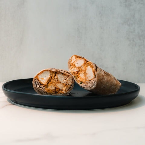 A dark plate on a light surface holds a Cheesy Garlic Chicken Wrap, cut in half and filled with seasoned chicken, with a neutral background.