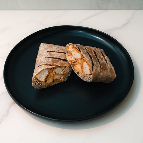 Two halves of the Cheesy Garlic Chicken Wrap, filled with chicken, are side by side on a black plate over white marble—a delicious high-protein meal prep option.