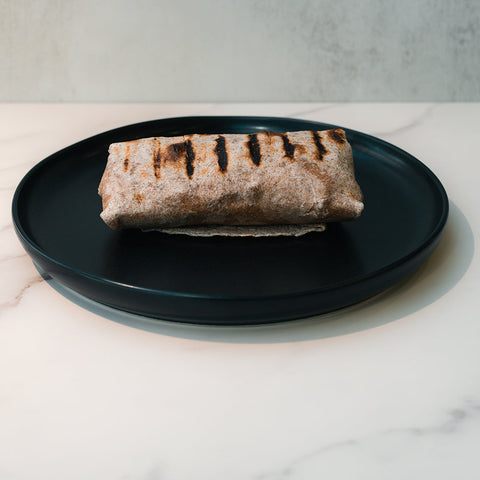 A Cheesy Garlic Chicken Wrap with char marks is served on a black plate atop a white marble surface, set against a light gray background.