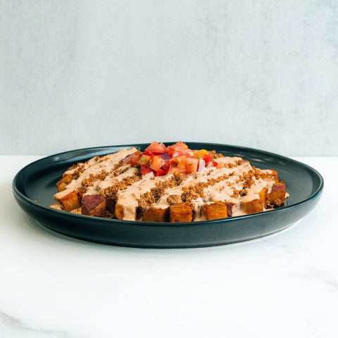 A black plate with TexMex Potato Hash topped with creamy sauce, crumbled seasoning, and a fresh diced tomato and herb garnish—ideal for high-protein meal prep or as a flavorful gluten-free Tex-Mex dinner.