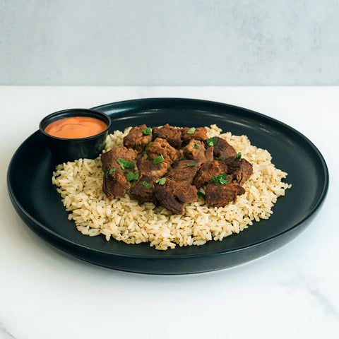 GLORIOUS GAINS Steak Bites Cilantro Lime Rice features juicy steak bites over cilantro lime rice, garnished with herbs and served with orange dipping sauce—a delicious, high-protein meal prep or bowl option.