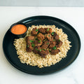 GLORIOUS GAINS Steak Bites Cilantro Lime Rice features cooked beef bites over cilantro lime rice, garnished with herbs and served with an orange dipping sauce—a perfect high-protein meal prep bowl.