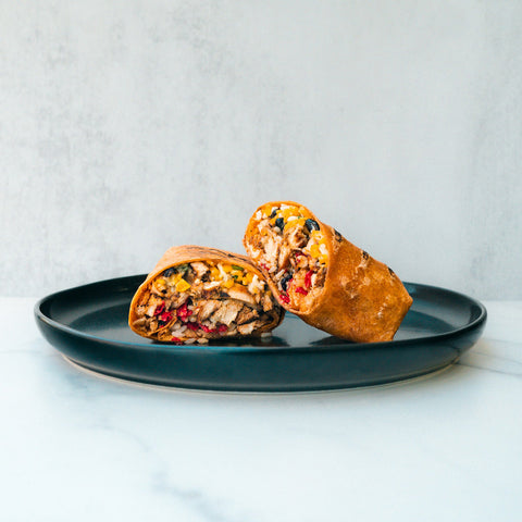 The Hey Arnold Burrito Subscription is a high-protein chicken burrito, sliced to showcase its hearty filling of meat, beans, rice, corn, and vegetables on a dark plate with a light background.