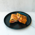 The Hey Arnold Burrito Subscription is a high-protein grilled wrap with chicken, corn, black beans, and red peppers—halved on a round black plate—making it an ideal post-workout meal.