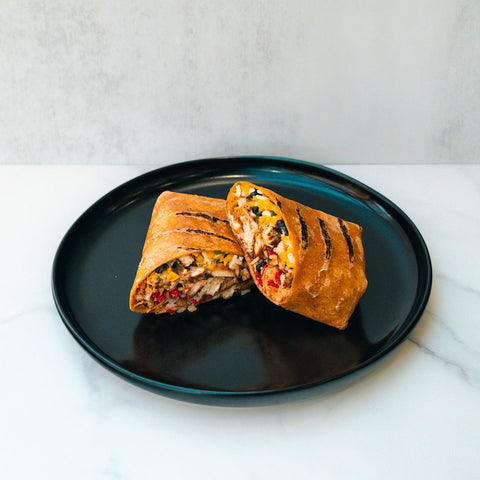 The Hey Arnold Burrito Subscription is a high-protein grilled wrap with chicken, corn, black beans, and red peppers—halved on a round black plate—making it an ideal post-workout meal.