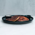 Cinnamon Roll Pancakes are served on a black plate with golden brown tops, accompanied by two small black cups of sugar free syrup and cream, all set against a white surface and light gray background.